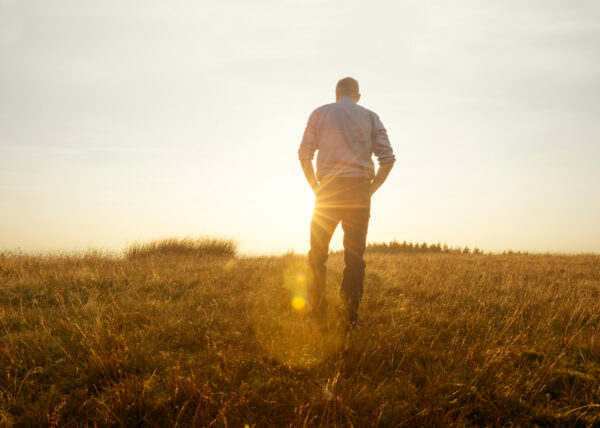 man standing in field looking away at sunset